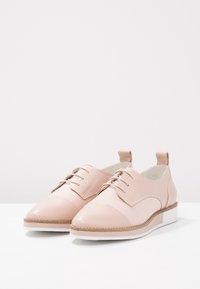 Scarpe in pelle rosa chiaro con puntatonda, design con lacci e suola bianca. Presentano una parte superiore testurizzata e dettagli di cucitura a contrasto.