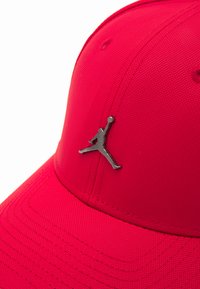Boné de basebol vermelho feito de tecido texturizado, apresentando um logo Jumpman prateado na frente. O design possui detalhes bordados ao redor da aba.