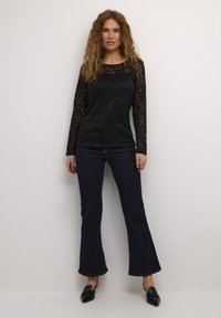 Černý dlouhý rukáv se zdobením krajkou, spárovaný s tmavými širokými džíny. Modelka má na sobě černé slip-on boty se čtveratým designem.