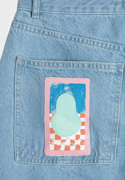 Bolsillo de mezclilla azul claro con un parche pintado que presenta una forma de pera verde sobre un patrón de tablero de ajedrez rojo y blanco con fondo azul.