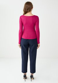 Strakke top met lange mouwen van felroze geribd stof, gecombineerd met marineblauwe broek en stijlvolle zwarte hoge hakken.