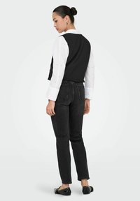 Zwarte cropped top over een witte shirt met oogjesborduursel, gecombineerd met hoge taille zwarte denim jeans en platte zwarte schoenen.