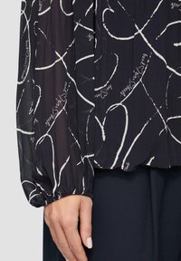 Blusa trasparente blu navy con stampa astratta a cuore bianco e testo in corsivo. Maniche arricciate, tessuto leggero e vestibilità morbida.