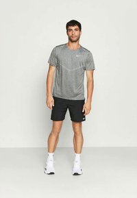 Γκρι αθλητικό T-shirt με διακριτική υφή, σε συνδυασμό με μαύρα σορτς. Και τα δύο είδη διαθέτουν το λογότυπο της Nike σε λευκό χρώμα. Φοριέται με λευκά αθλητικά παπούτσια.