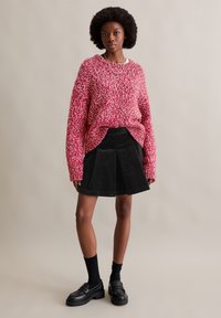 Rot und weiß gestrickter Pullover mit oversize Schnitt, kombiniert mit einem schwarzen Cord-Rock mit Falten, schwarzen Socken und Plateauschlüpfern.
