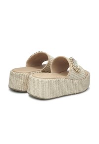 Sandali piattaforma beige intrecciati con una finitura testurizzata, caratterizzati da un grande gioiello decorativo sulla cinghia e un design a schienale aperto.