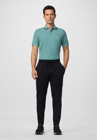 Helles Teal-Polohemd mit Kragen, schwarze Jogginghose und schwarze Sneakers. Enthält drei weiße Streifen an den Ärmeln und Logo-Detail.