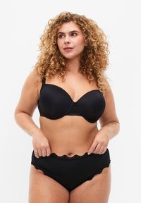 Completo di lingerie nera con reggiseno balconette imbottito e rifiniture in pizzo, abbinato a culotte a vita alta. Tessuto liscio con bordi a onda.