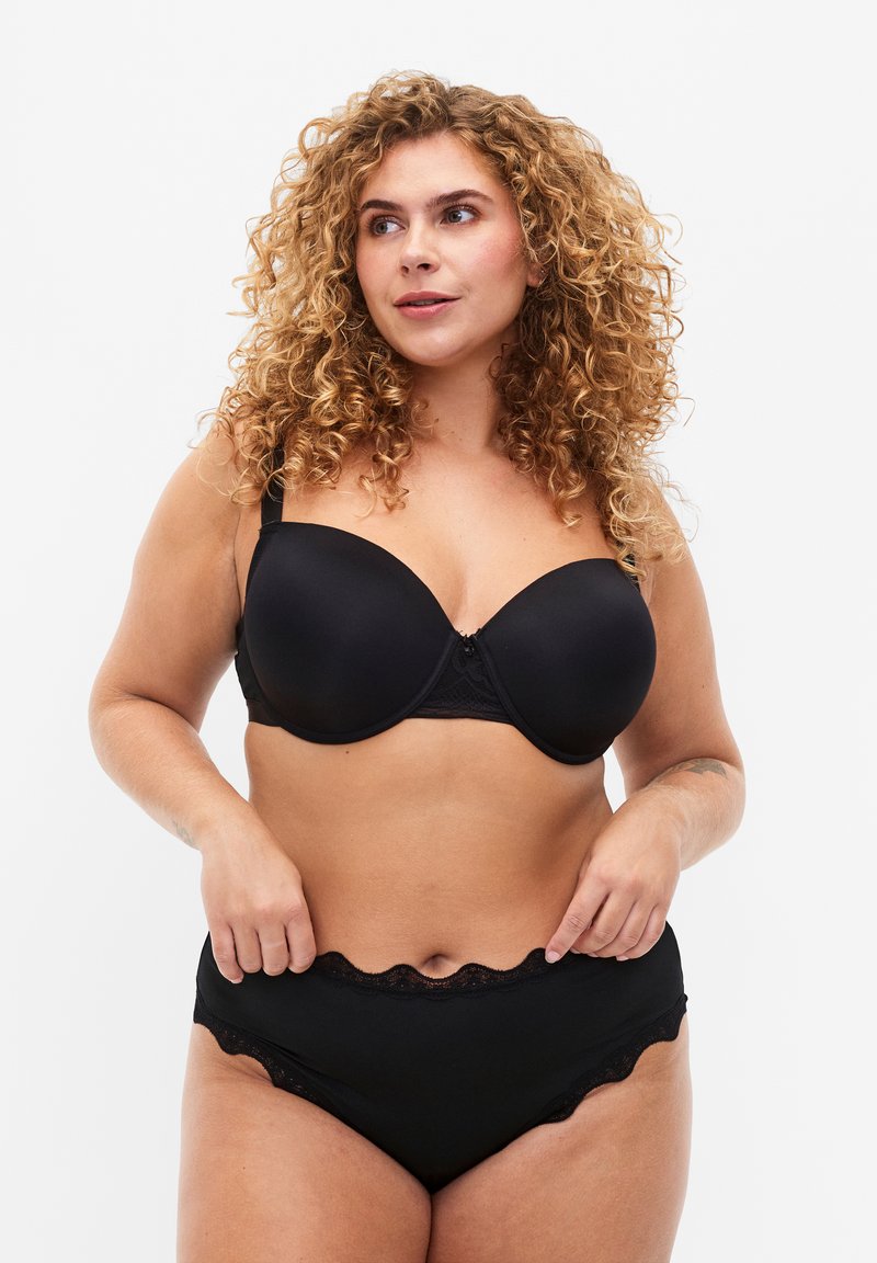 Completo di lingerie nera con reggiseno balconette imbottito e rifiniture in pizzo, abbinato a culotte a vita alta. Tessuto liscio con bordi a onda.