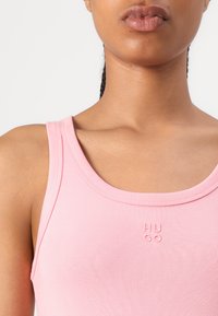 Débardeur rose clair côtelé avec un col rond et un logo brodé discret, affichant une coupe ajustée et une texture lisse.