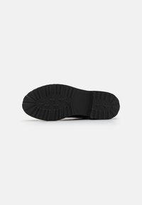 Black rubber shoe sole features deep treads and a rounded design, with ridges along the edges for traction and durability.