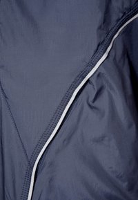 Tejido azul marino con una textura sutil; presenta costuras blancas a lo largo de la costura en ángulo para hacer contraste. Material suave y ligero.