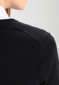 Schwarzer gestrickter Pullover mit glatter Textur, runder Halslinie und subtilen Nahtdetails an der Schulter und im Rücken.