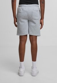 Grå bomuldsshorts med elastisk talje og en enkelt baglomme, parret med hvide sneakers og ankelsokker.