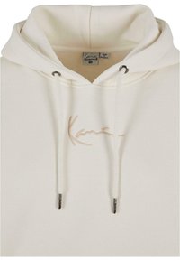 Cream-colored hoodie made from soft fabric, featuring a drawstring hood and silver-tone aglets. Includes light beige embroidered branding.