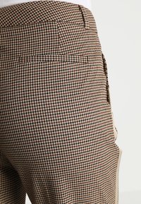 Bruna och beige rutiga byxor med en slät yta, som har en bakficka och en åtsittande design.