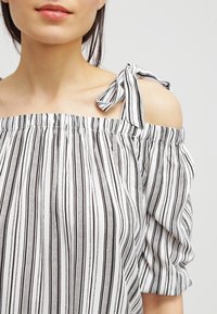 Off-the-shoulder topp i lättviktig tyg, med svarta och vita vertikala ränder, elastisk halsringning och knytband.