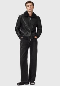 Sort læder bomberjakke med en shearling-krave, frontlynlås og to sidelommer, kombineret med brede mørke jeans og sorte ankelstøvler.