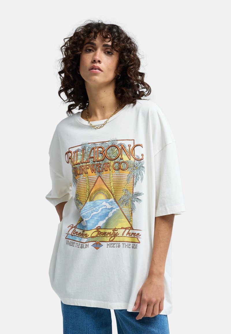 T-shirt blanc surdimensionné présentant un design graphique coloré avec une pyramide, des palmiers et des vagues océaniques, fabriqué en tissu de coton doux.