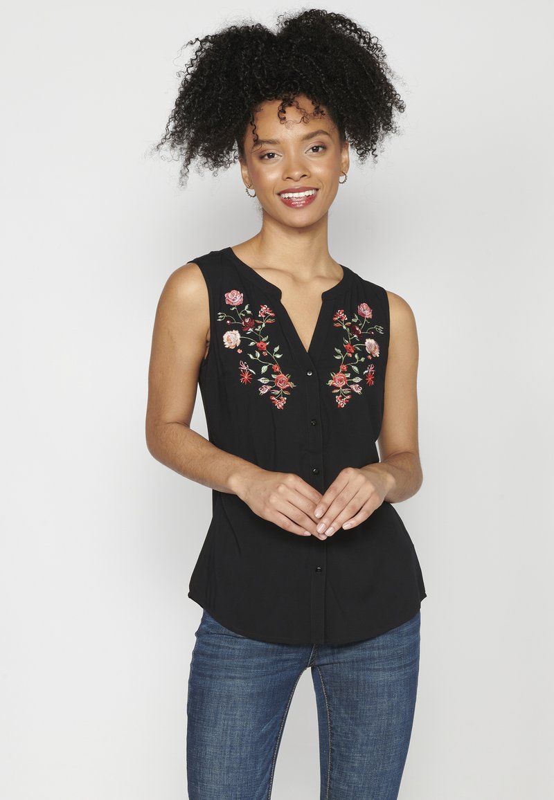 Camiseta sin mangas negra con bordado floral en tonos de rosa y verde. Presenta un escote en V y un cierre frontal de botones con dobladillo redondeado.