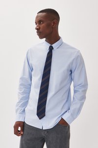  Lichtblauw overhemd met lange mouwen, gecombineerd met een marineblauwe stropdas met diagonale strepen in beige. Grijze jeans maken de outfit compleet.
