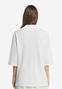 Hvid kortærmet polo-shirt, afslappet pasform, ren krave, glat tekstur og ingen synlige mønstre eller accenter set fra bagagen.
