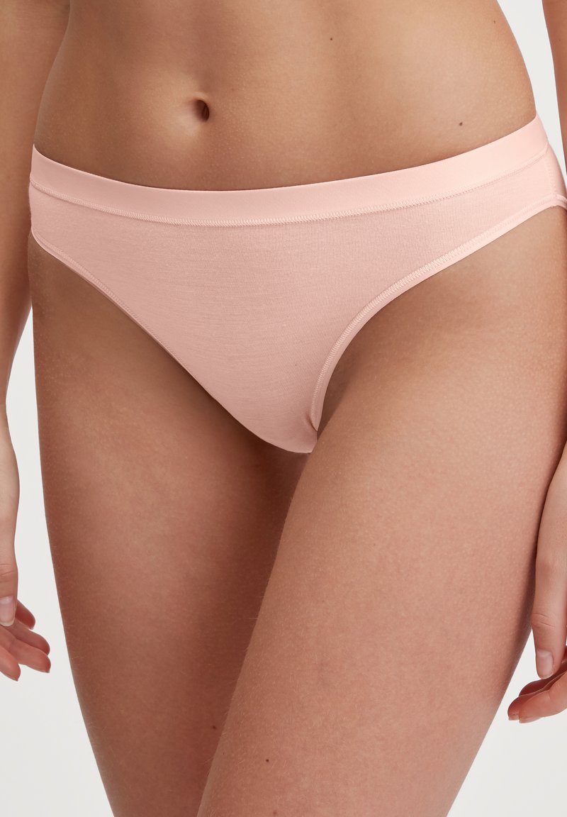 Lichtroze katoenen tanga met een naadloze tailleband. Zachte textuur met subtiele stikseldetails langs de randen, ontworpen voor comfort.