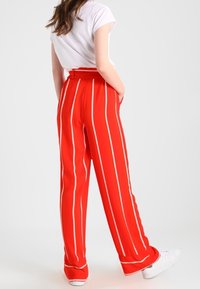 Rood gestreepte broek met een hoge taille, voorzien van witte verticale lijnen en een wijde pijpenontwerp, gecombineerd met witte sneakers.