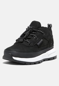 Zapatillas deportivas negras con un upper texturizado, una gruesa entresuela blanca y una suela de goma negra; cuentan con cordones elásticos y una pestaña de sujeción.