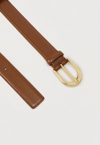 Rjav pas iz usnja z gladko teksturo, z zlatim kovinskim zaponkom v obliki črke U. Pas ima vidne šive in en zatič.