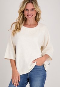 Licht crèmekleurige oversized gebreide trui met een ronde halslijn en klokmouwen, met een zachte textuur en zijsplitten, gedragen met blauwe jeans.