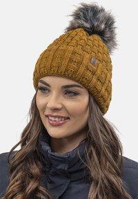 Gorro de lana color mostaza con un patrón texturizado y un pompón de piel sintética en la parte superior. Parche de cuero con logo en la parte delantera.