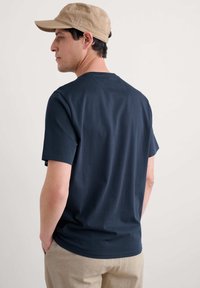 Camiseta de manga corta azul marino de algodón con cuello redondo, combinada con pantalones beige claros y una gorra beige.