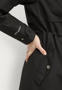 Giacca nera con una vestibilità sartoriale, caratterizzata da un elegante polsino con logo ricamato, un bottone a scatto e un dettaglio con tasca laterale.