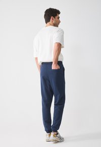Marineblå joggebukser med elastisk liv, sidelommer og ribbestrikkede mansjetter; kombinert med hvit t-skjorte og joggesko.