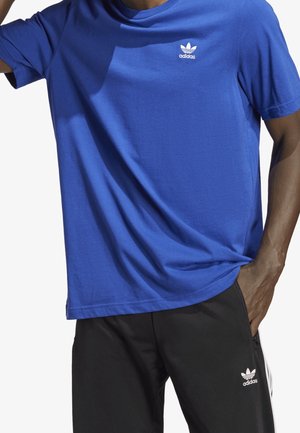 Modré bavlněné tričko s kulatým výstřihem a krátkými rukávy. Bílé logo Adidas na hrudi. V kombinaci s černými kalhotami s bílým logem.
