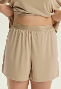 Beżowe szorty z elastycznym pasem, o luźnym kroju, wykonane z miękkiego materiału. Posiadają boczne rozcięcia, które ułatwiają ruch oraz subtelne detale w szwach.