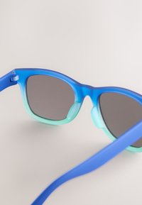 Blauw-groene gradientzonnebril met afgeronde monturen, donkere glazen en zachte neusstukken. Heeft een gladde, matte afwerking.