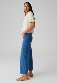 Maglione fuzzy beige chiaro, jeans a vita alta blu a gamba larga e ballerine beige. Design semplice con cuciture minime e tasche frontali.