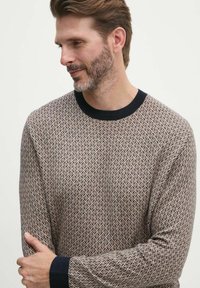 Maglione lavorato a maglia con un motivo geometrico in beige e marrone, con un collo a girocollo e polsini a costine blu navy. Tessuto morbido.
