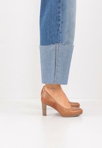Escarpins en cuir marron à bout rond et talon empilé, associés à un jean denim bleu clair court avec ourlet effiloché.