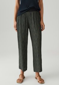Pantaloni a palazzo neri e verdi con motivo a foglie, realizzati in tessuto leggero e con una vestibilità comoda. Abbinati a sandali flat.