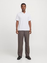 Polo shirt blanc avec un motif texturé, à manches courtes et col, associé à un pantalon ample gris foncé et des chaussures noires.