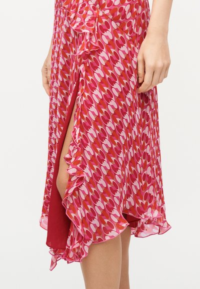 Κοντινό πλάνο φούστας με μοτίβο σε ροζ και κόκκινους τόνους με βολάν στις άκρες, που ανοίγει μερικώς για να αποκαλύψει ένα πόδι.