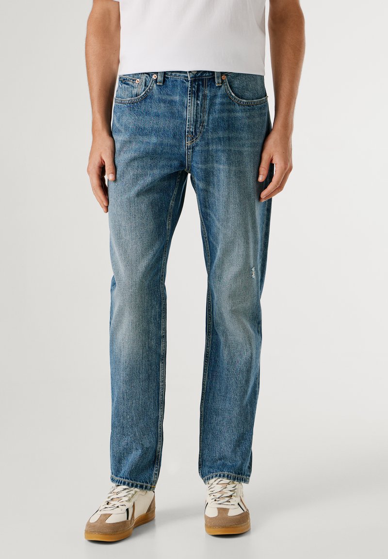 Heledad hallid teksad sirge säärega, nähtava õmblusega ja kerge tuhmumisega. Omab eesmine taskuid ja nööbiga sulgemist.