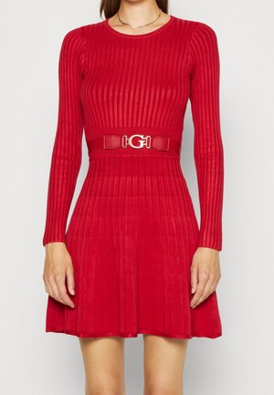 Femme portant une robe en maille côtelée rouge à manches longues et une ceinture assortie avec une boucle dorée à la taille.