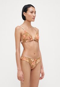 Bikini a stampa floreale con top triangolare e slip a vita bassa, caratterizzato da tonalità beige e rosa soffice, texture a coste e spalline sottili.