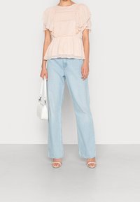 Blouse rose clair à pois, avec des volants superposés et une couture à la taille, assortie à un jean large bleu clair et un sac à main blanc.