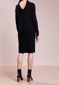 Vestito lavorato a maglia nero con scollatura a V profonda, maniche lunghe e silhouette aderente. Abbinato a stivaletti neri con tacco in stampa leopardata.