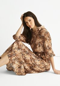 Leopard print shirt dress in shades of brown and beige, featuring a collar, long sleeves, and a tie at the waist. Soft, flowing fabric.